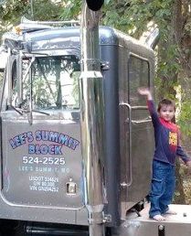 Child waving beside silver semi truck with “Lee’s Summer” logo on the door