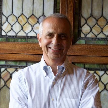 A man in a striped shirt is smiling in front of a stained glass window.