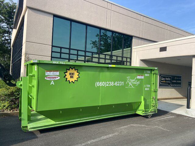 Green dumpster in front of a modern office building entrance