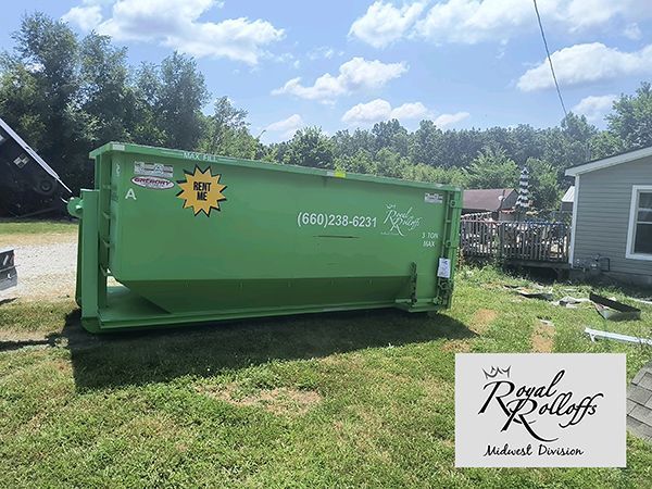 Two men shake hands beside a bright green dumpster at a house construction site.