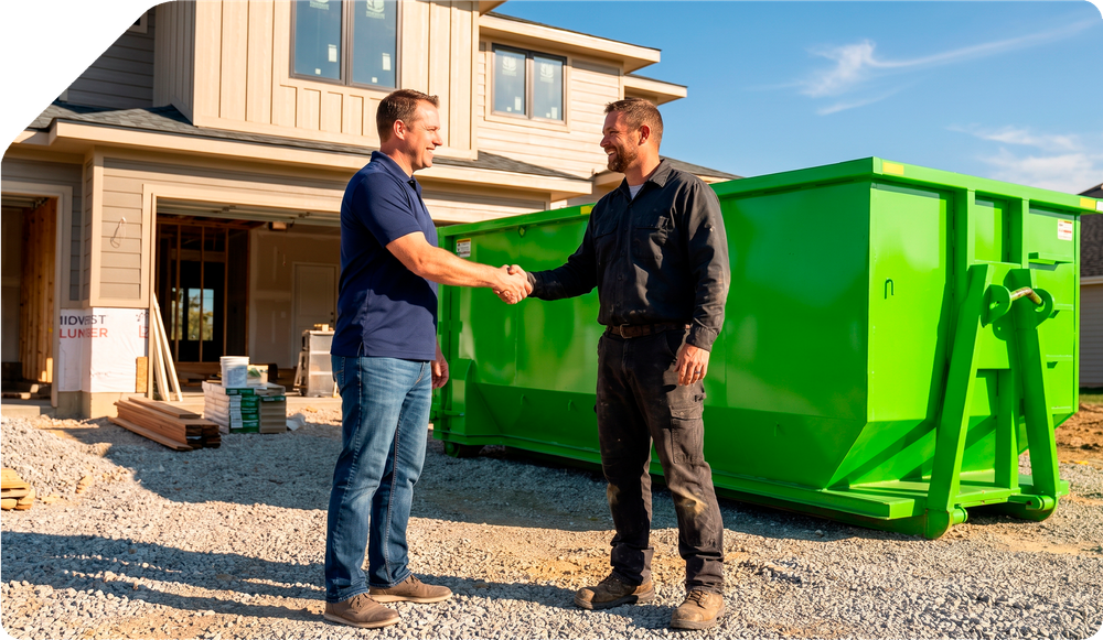 Two men shake hands beside a bright green dumpster at a house construction site.