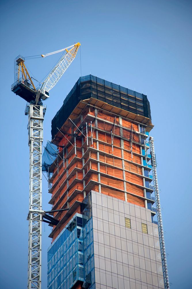 Construcción de un rascacielos con una grúa contra un cielo azul claro.