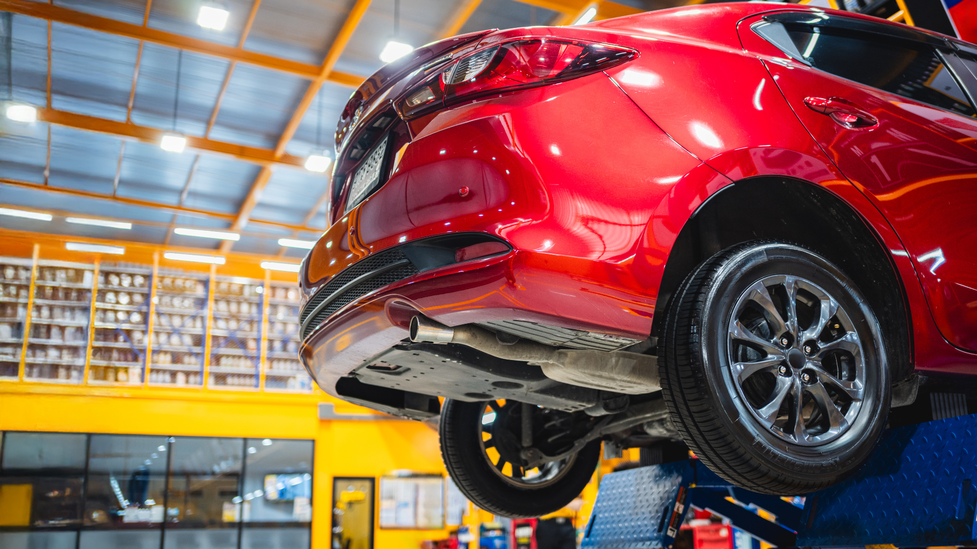 Red car lifted in a garage, showcasing undercarriage.