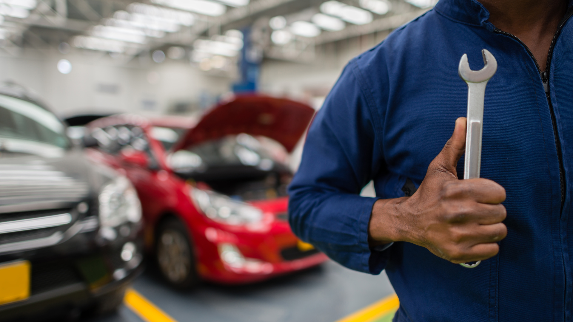 Mechanic holding a wrench in auto repair shop, red car in background.