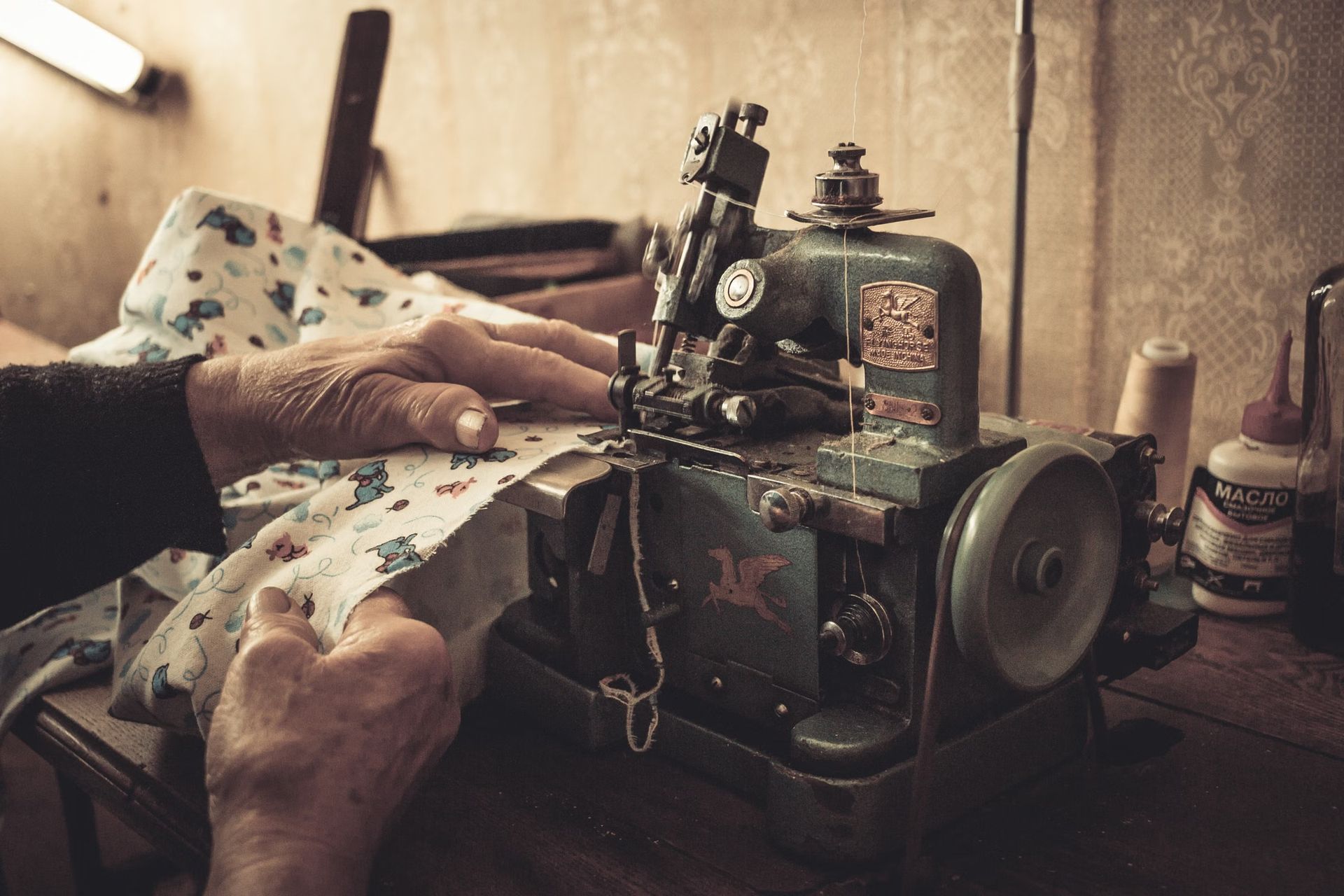 Hands guiding fabric under the needle of a sewing machine in warm low light