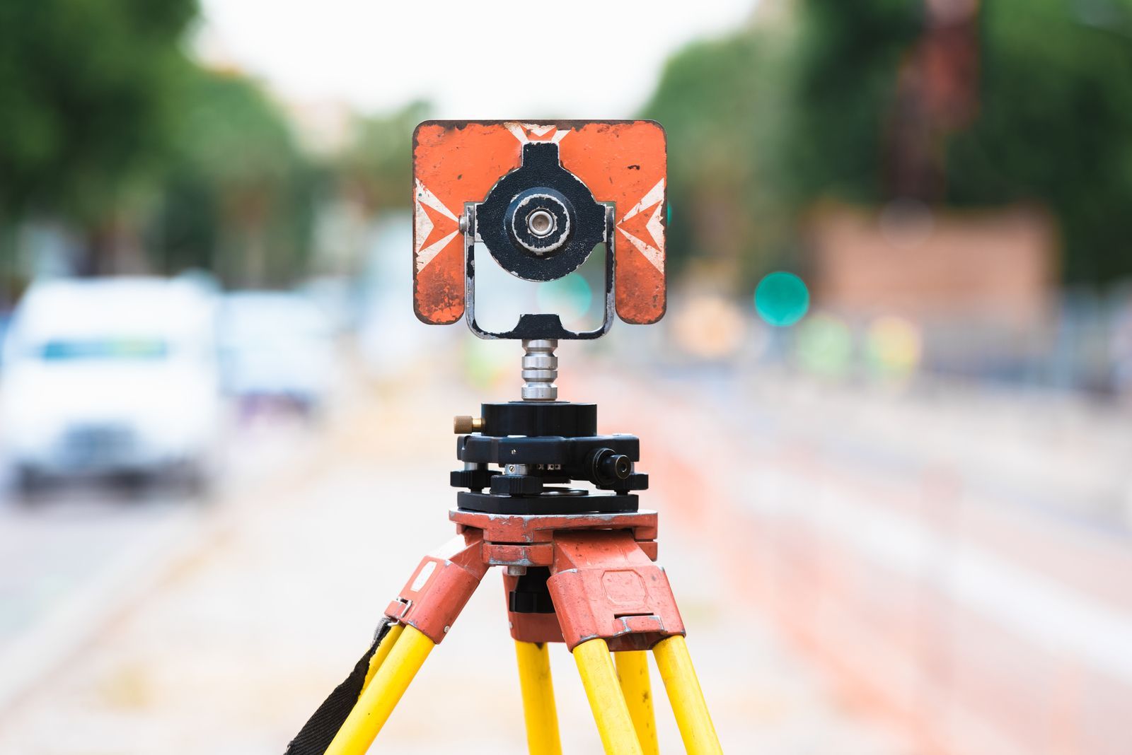 Surveying instrument on tripod, orange and white target, blurred street background.