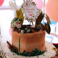 Birthday cake with pink frosting, tropical leaves, and “Happy 65th Birthday” topper