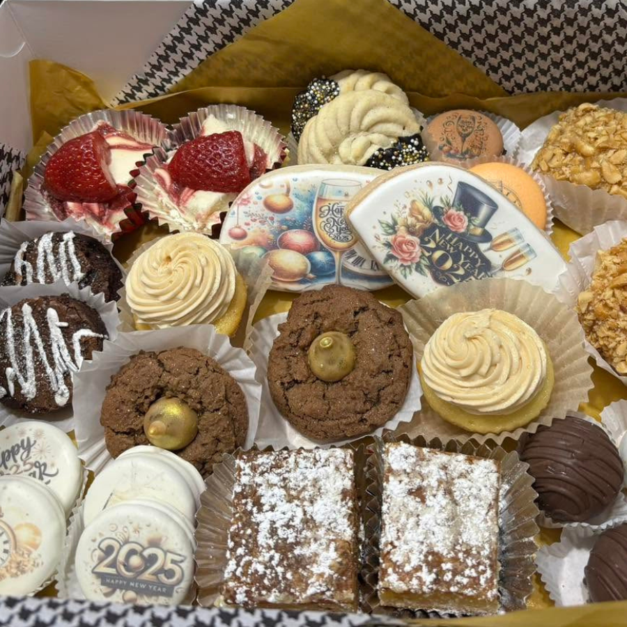 Assorted decorated cupcakes and dessert bars arranged in a box with floral decorative plates and gold accents