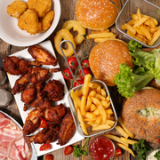 Assorted fast food spread with burgers, fries, chicken wings, nuggets, and dipping sauce on a table