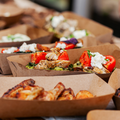 Tray of assorted pizza slices and appetizers in brown cardboard boxes, topped with tomatoes, cheese, and herbs