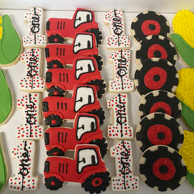 Assorted red tractor-shaped decorated cookies arranged in rows with black wheels and white icing details
