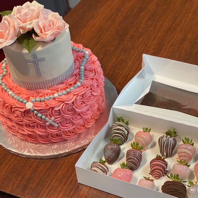 Pink frosted cake with roses and candy box of chocolate-covered strawberries on a wooden table