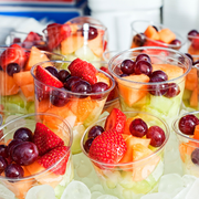 Clear cups of mixed fruit topped with strawberries, grapes, and cherries at a bright party display
