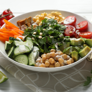 Colorful salad bowl with cucumbers, tomatoes, avocado, chickpeas, carrots, corn, and herbs