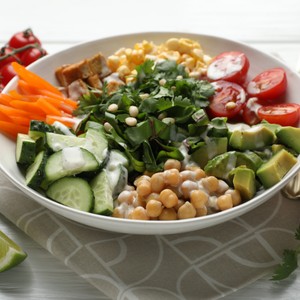 Colorful salad bowl with cucumbers, tomatoes, avocado, chickpeas, carrots, corn, and herbs
