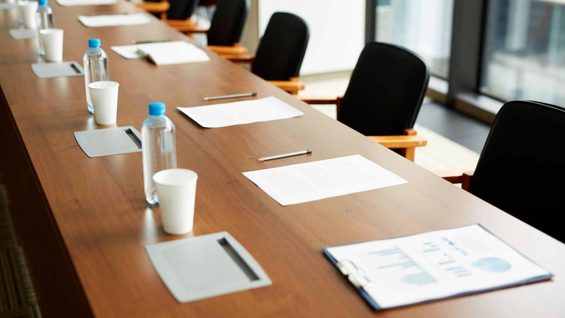 Conference table with papers, water bottles, and coffee cups in a bright meeting room.