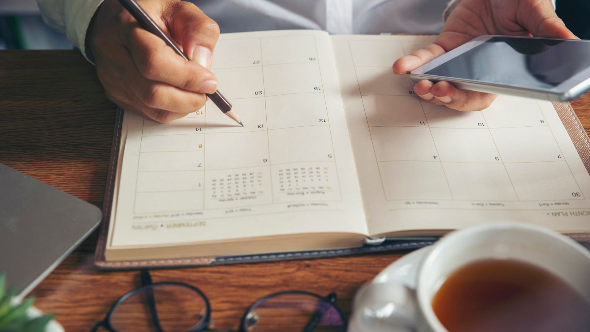 Hands sketching a floor plan on a notebook beside a smartphone and coffee cup on a desk