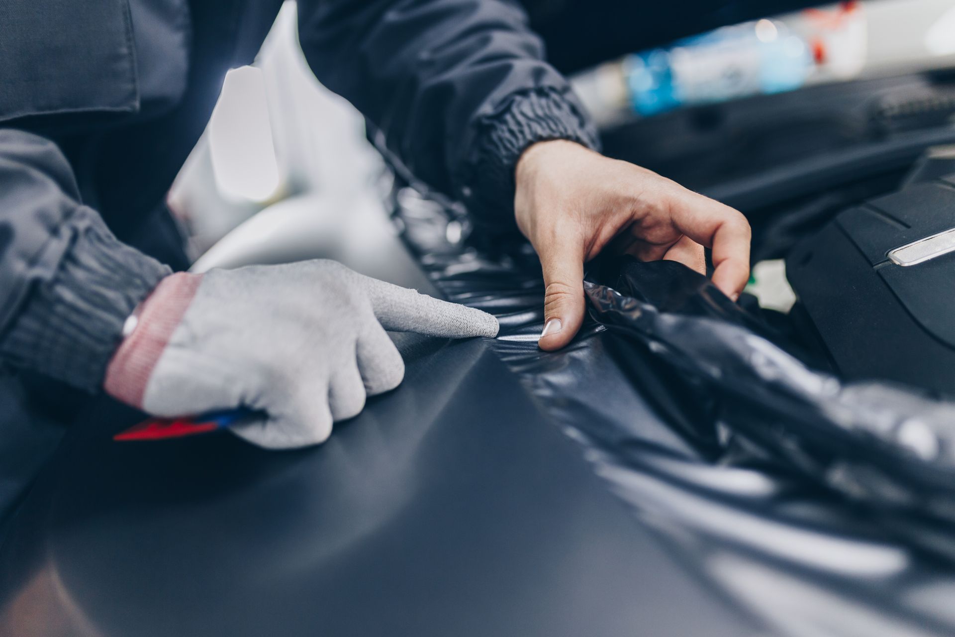 Hands in gloves applying a windshield repair tool to a car hood in a garage