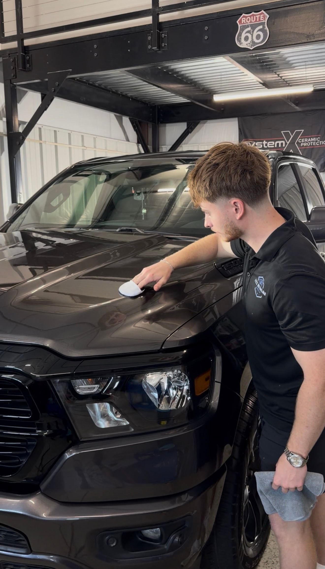 Person polishing the hood of a black SUV in a covered garage