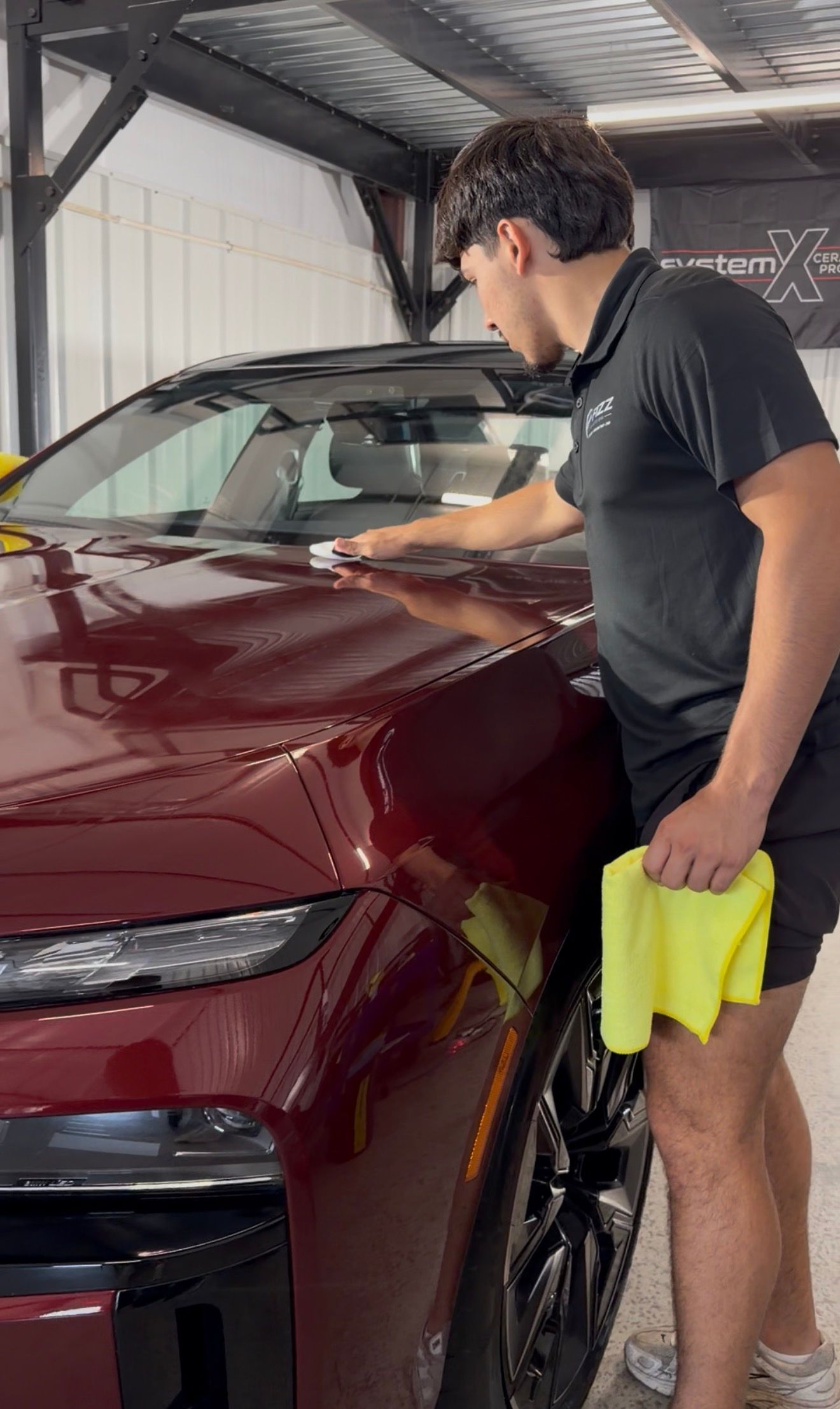 Person wipes a maroon car in a garage, holding a yellow cloth.