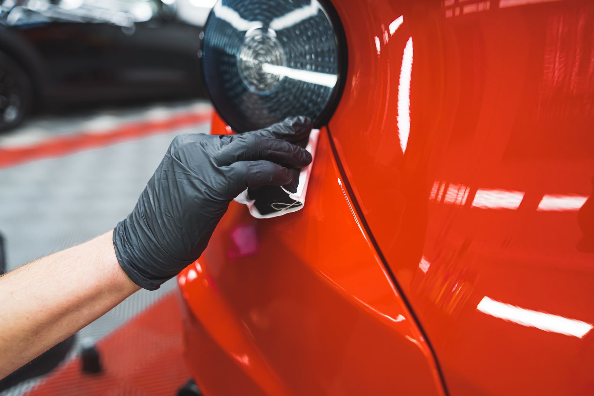 Hands peeling protective film from a black car headlight in a workshop