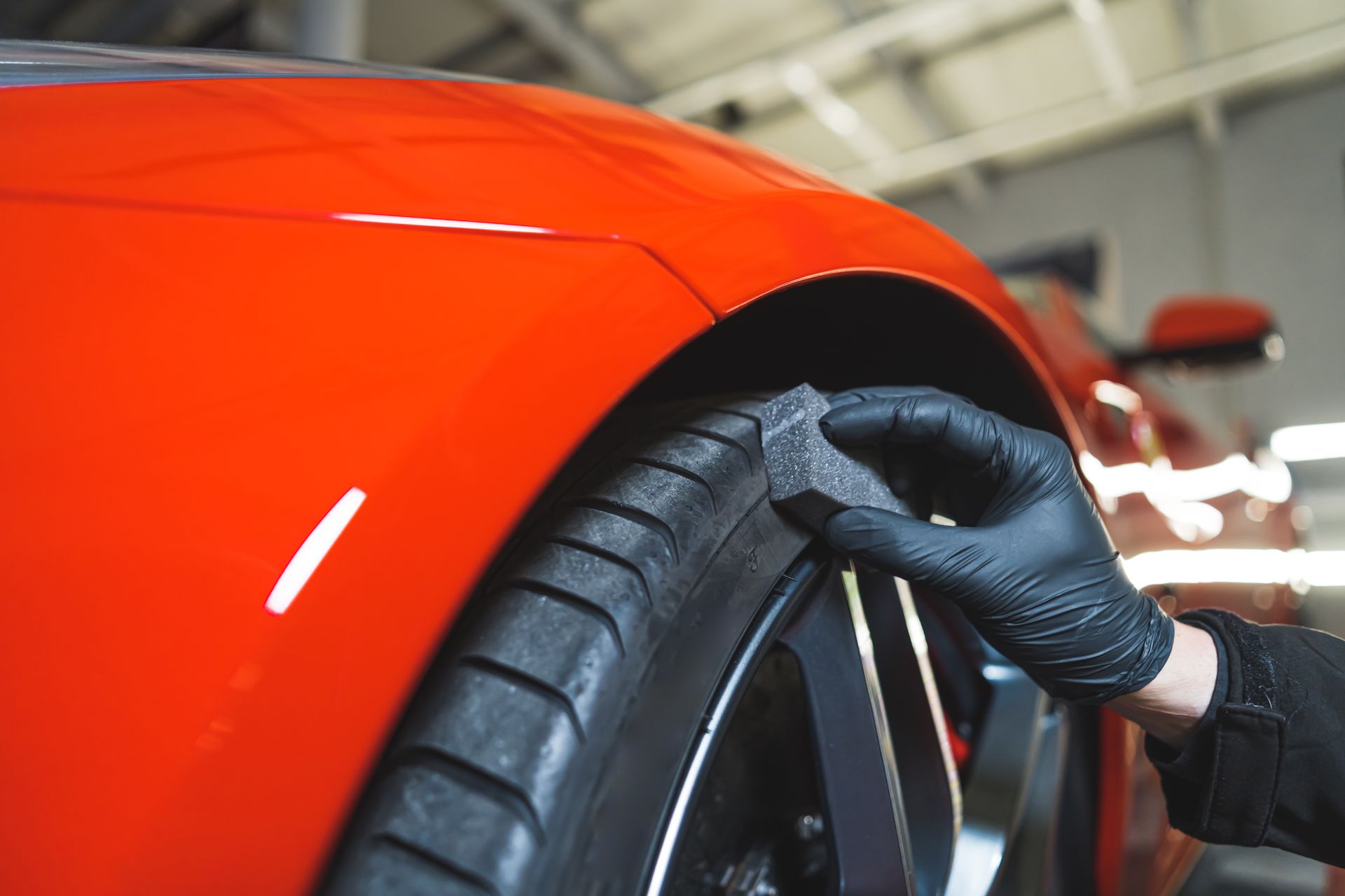 Gloved hand inspecting a car tire beside a red sports car in a garage