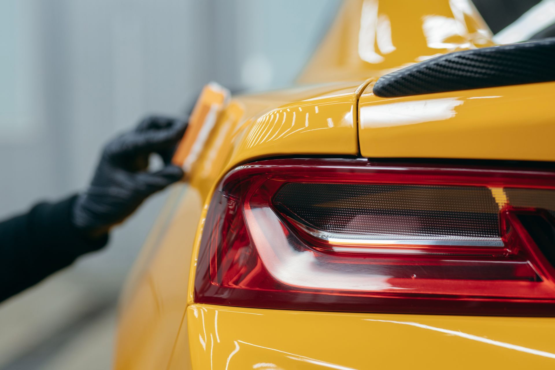 Black-gloved hand polishing the rear of a yellow sports car