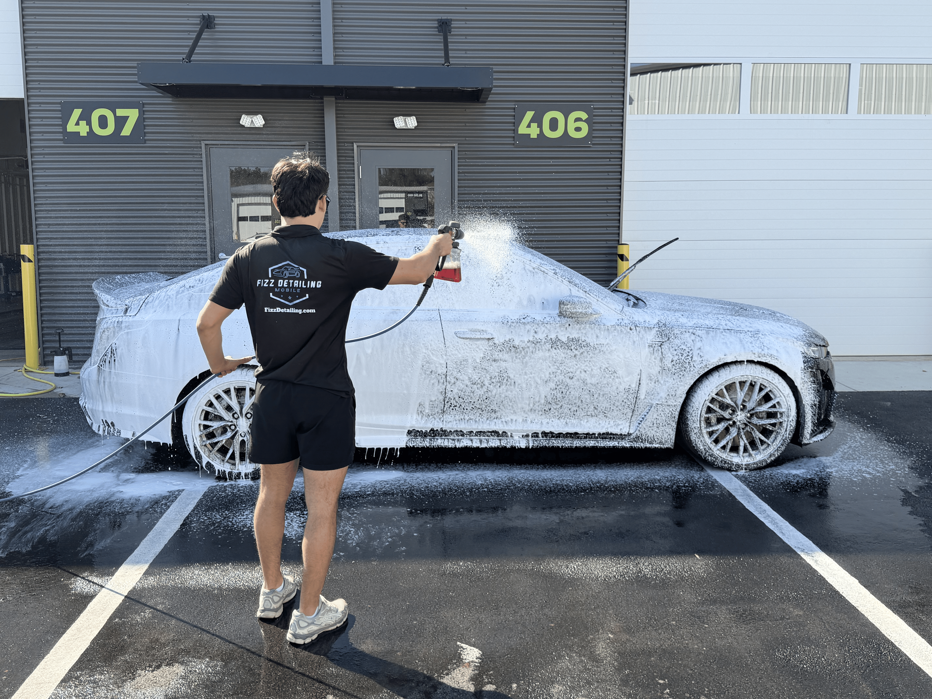 Person pressure-washing a white car outside garage doors 406 and 407.