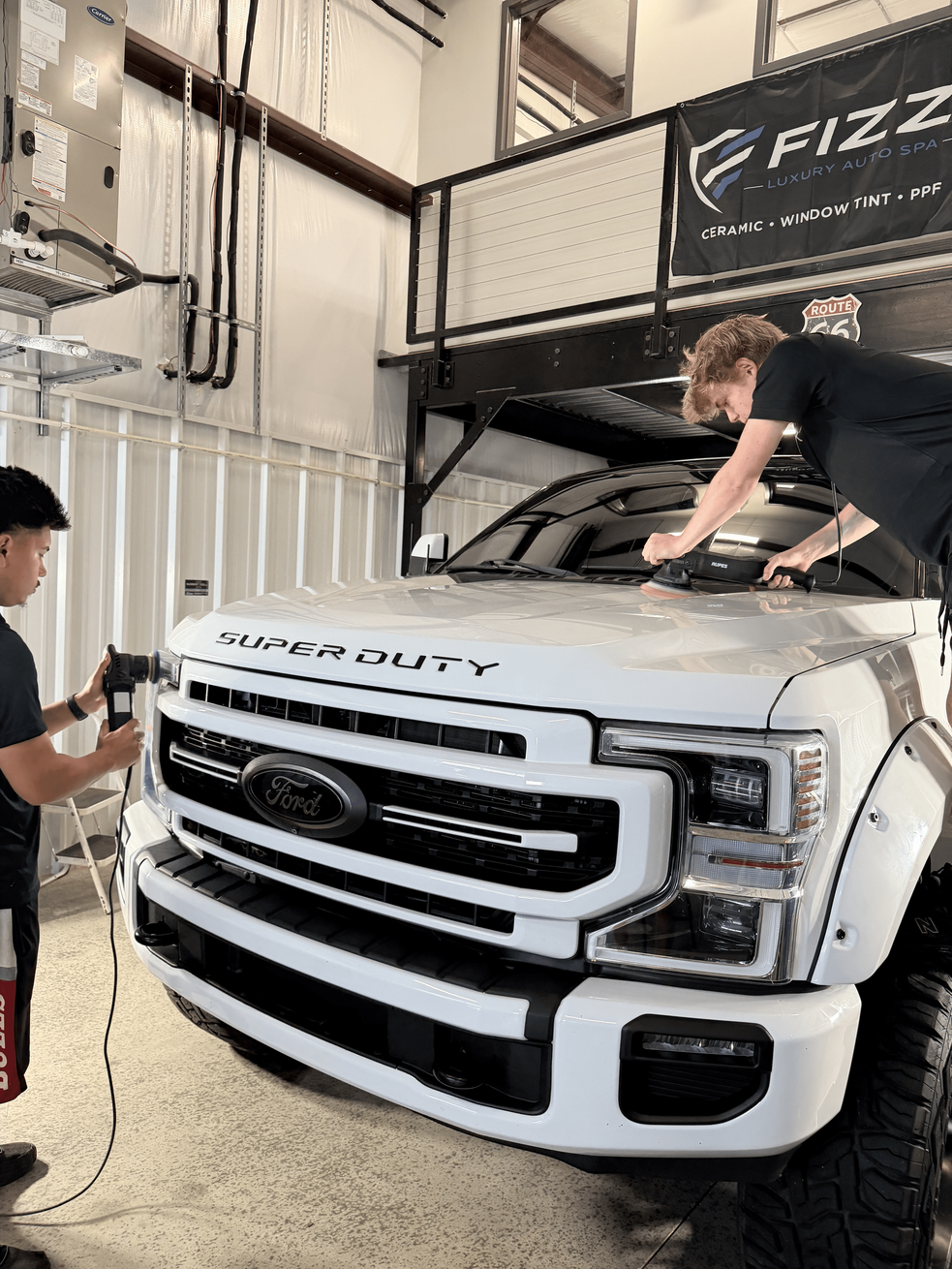 Two people washing a white pickup truck in a garage detail bay