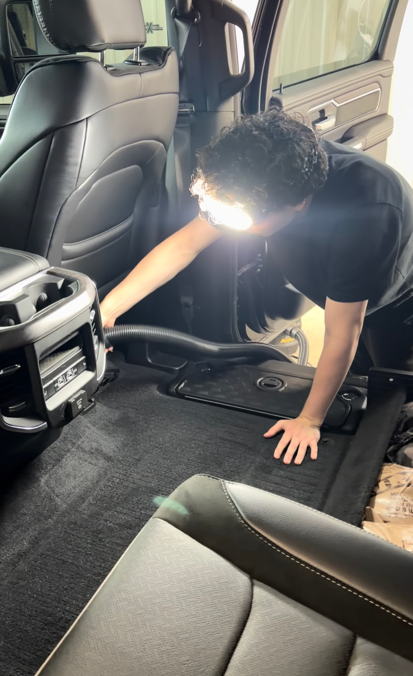 Person cleaning a car’s back seat area with a vacuum inside a dark interior.