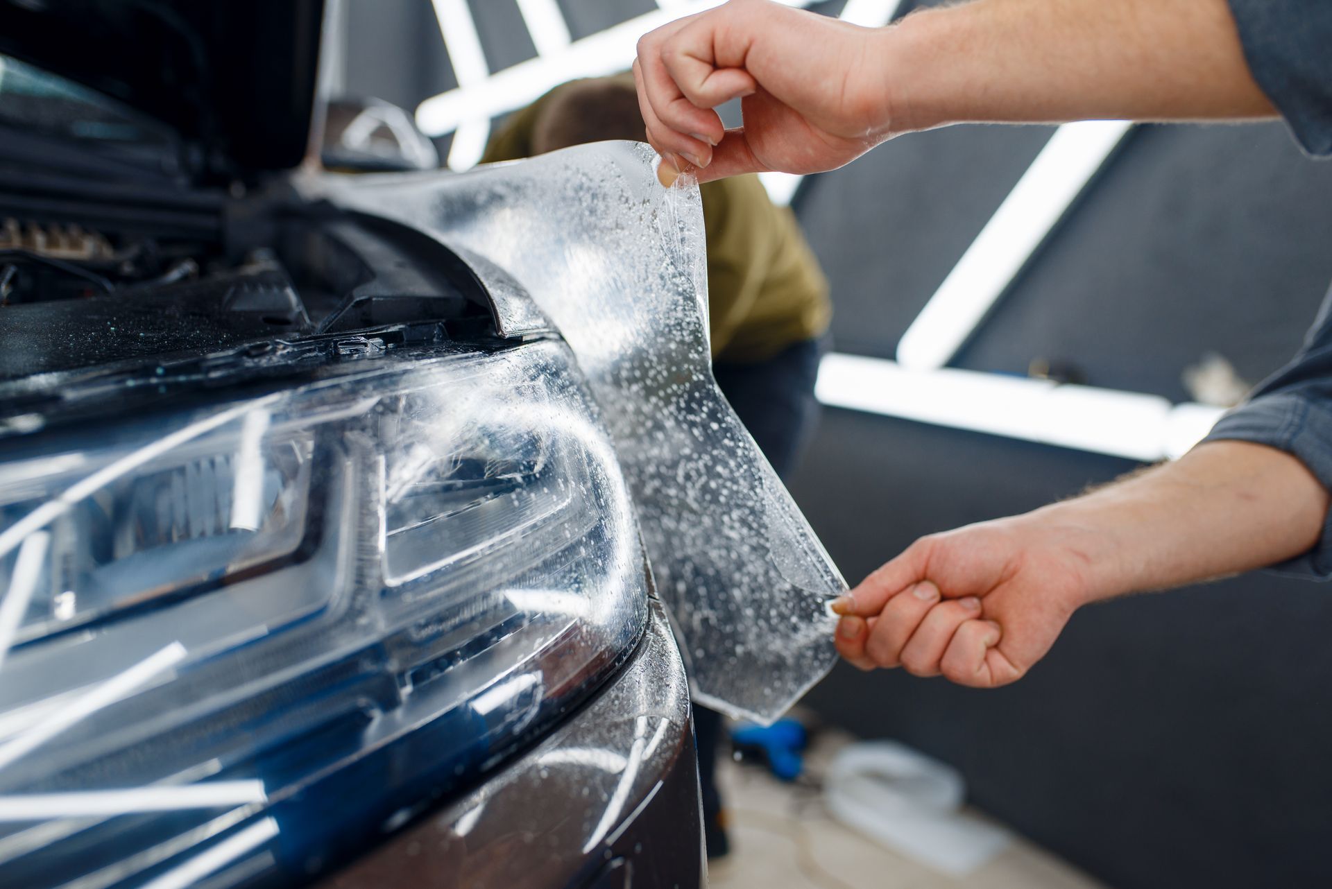 Hands applying car wrap to a glossy black vehicle in a workshop