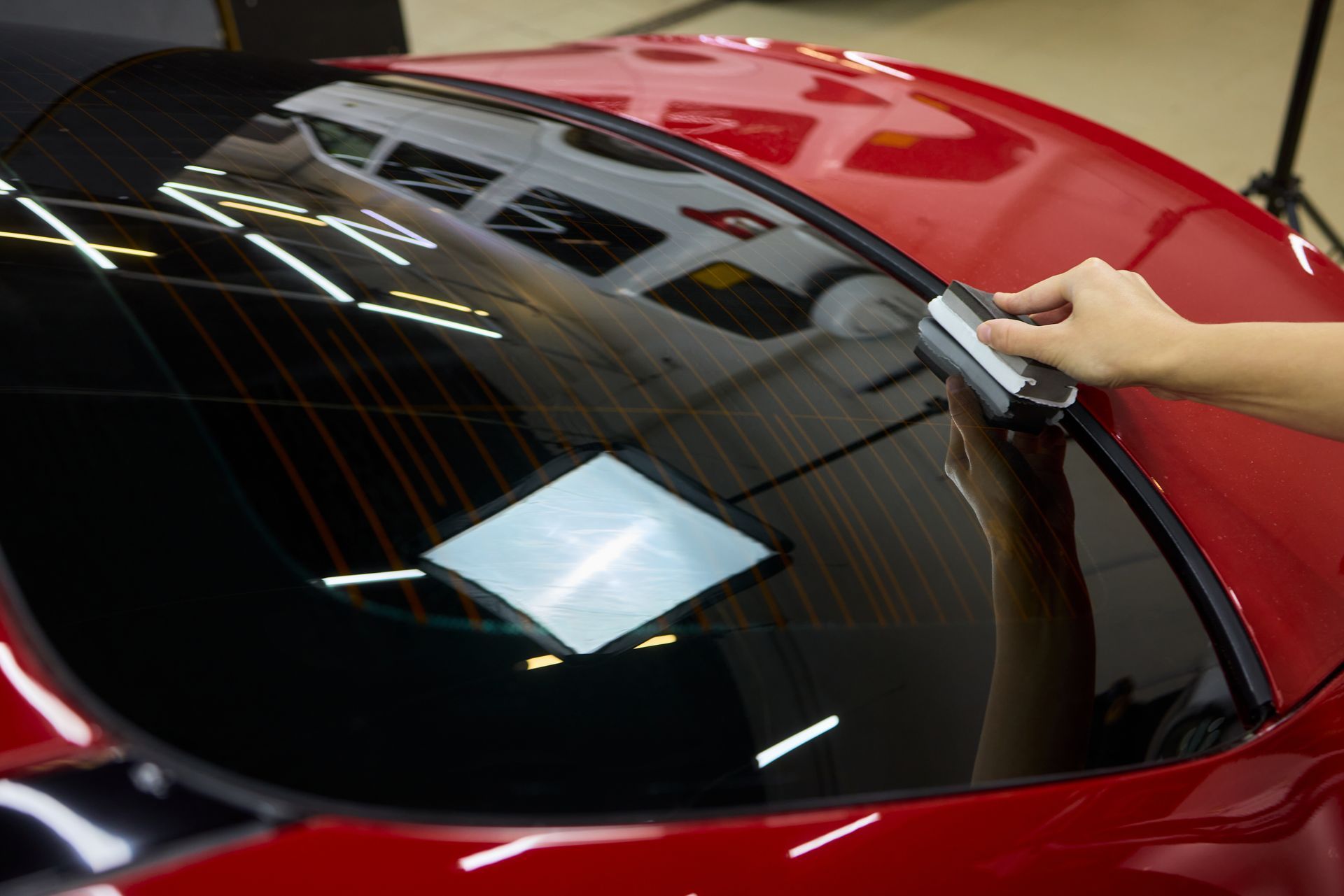 Hands peeling protective film from a black car headlight in a workshop