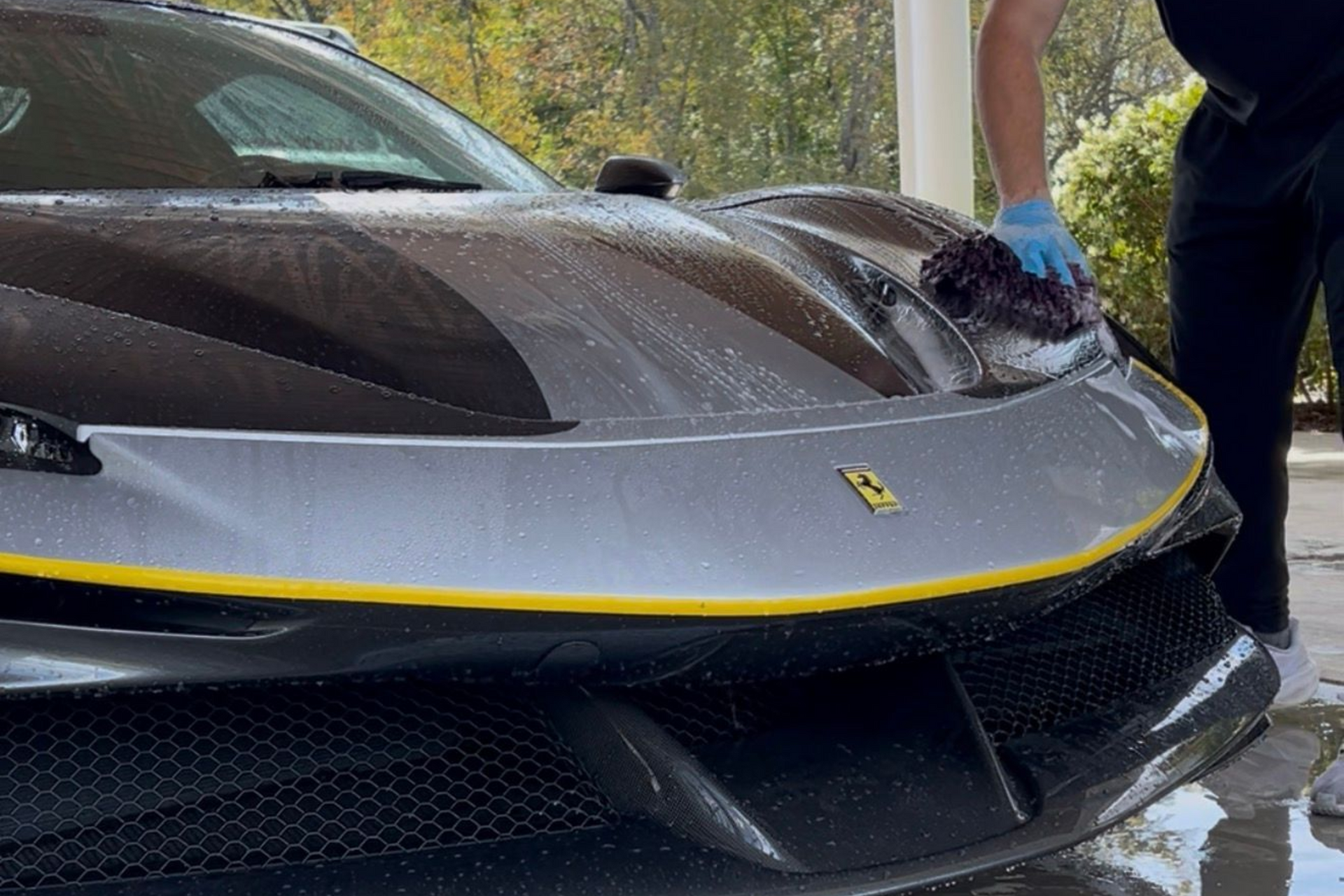 Black Ferrari front end in a wet driveway, with one person standing beside it.