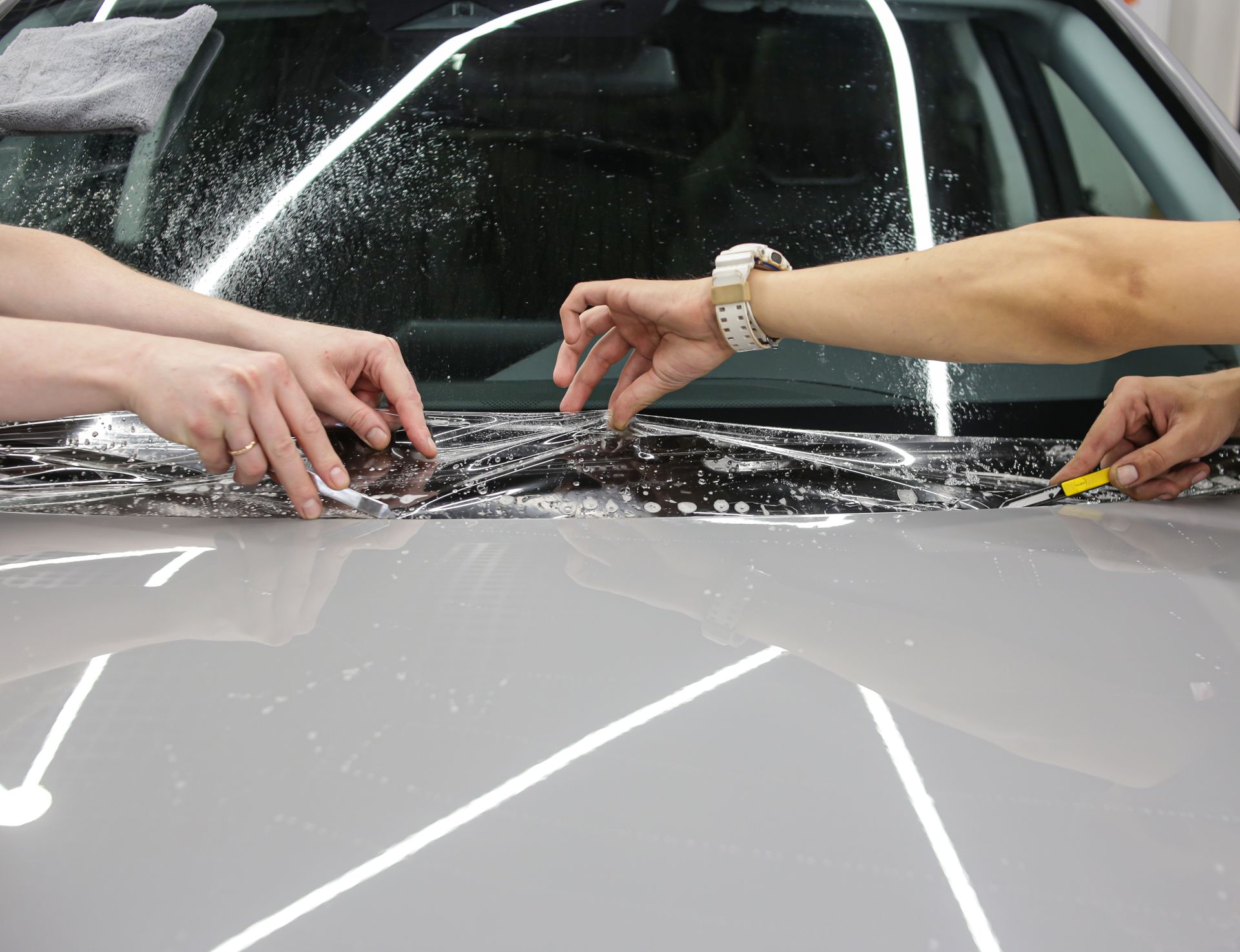 Hands peeling protective film from a black car headlight in a workshop