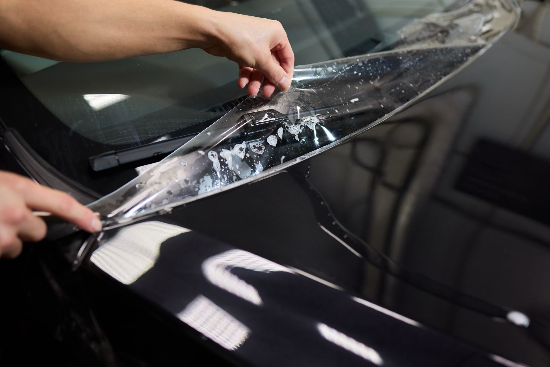 Hands peeling protective film from a black car headlight in a workshop