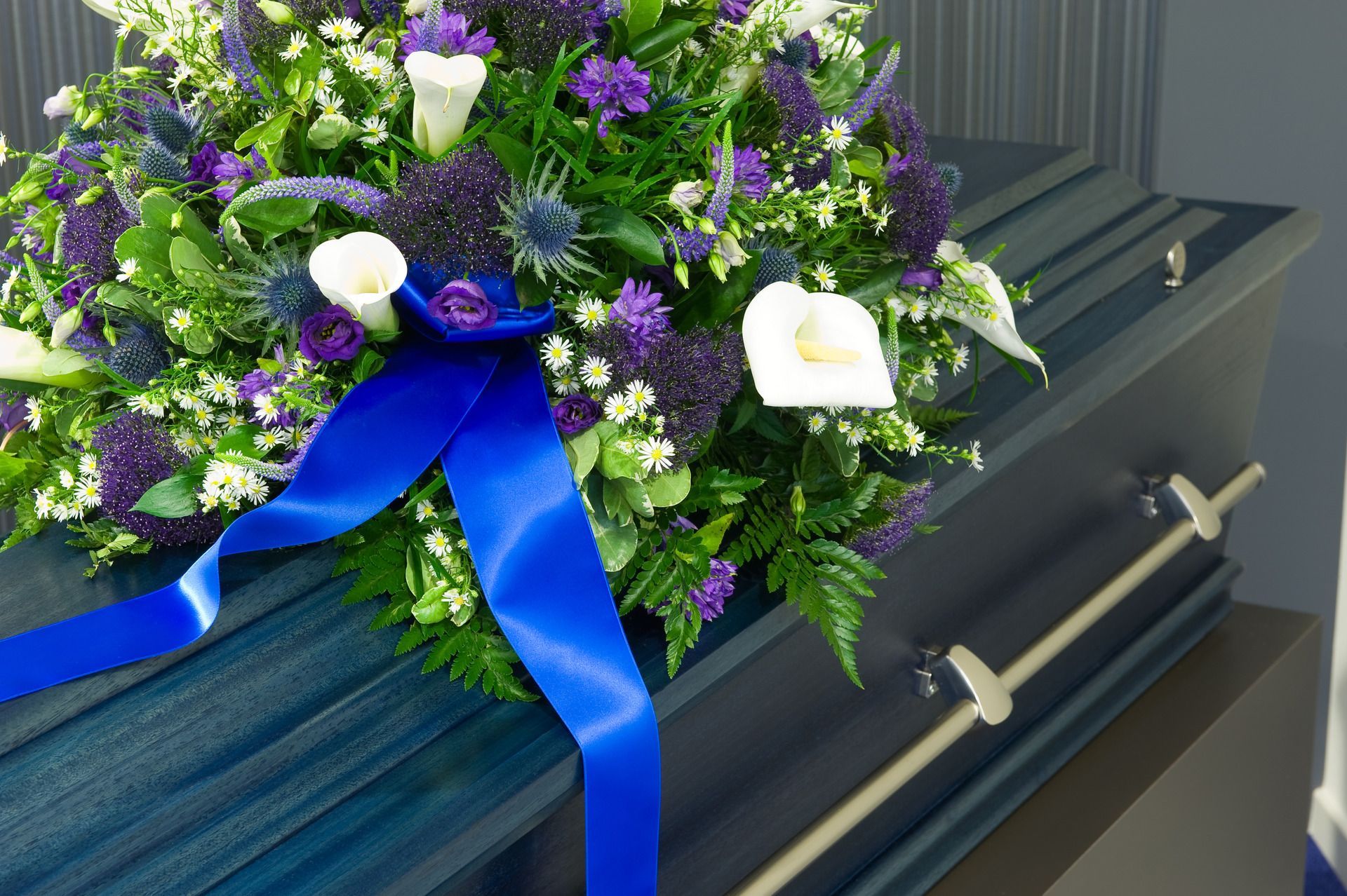 Purple and white funeral wreath with blue ribbon on a dark coffin