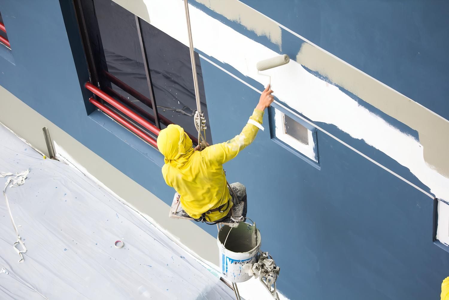 A Man in a Yellow Jacket is Painting a Building With a Roller — O'Brien Painting Contractors in Nambour, QLD