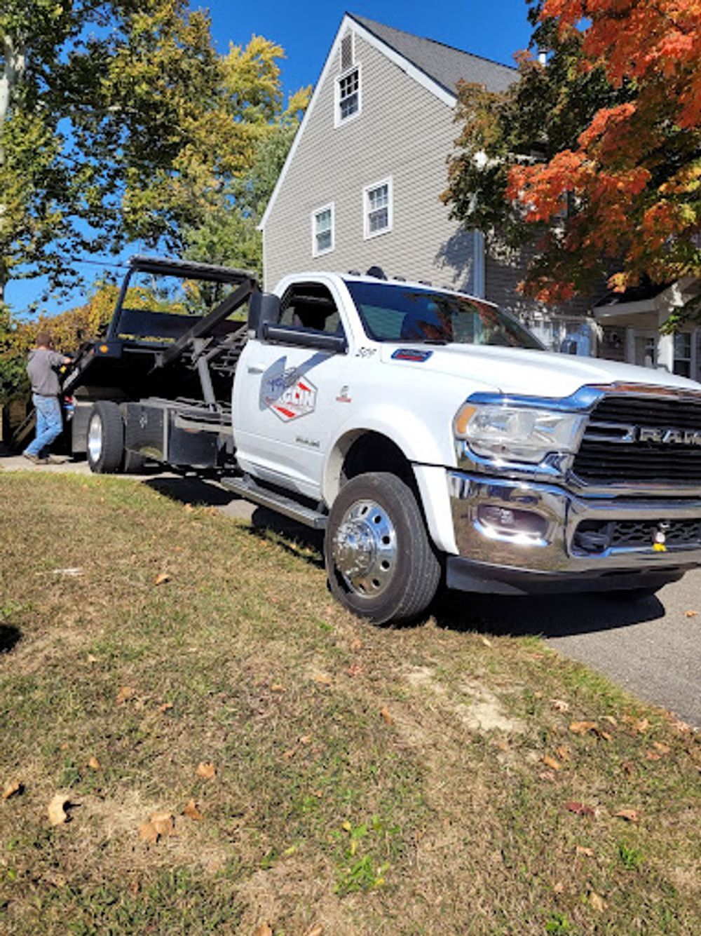 White tow truck on grass in front of a house, an operator is standing by the truck.