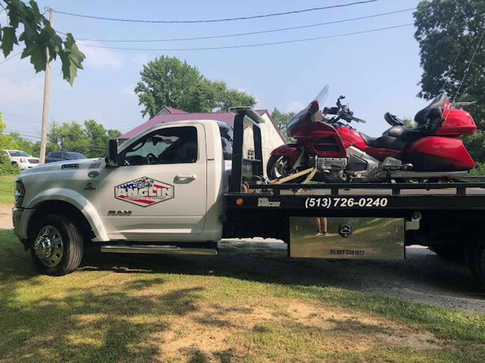 White tow truck with red motorcycle on the flatbed, parked on grass.  Anglin logo and phone number visible.