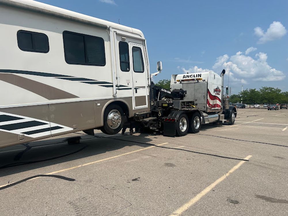 A large white and brown RV being towed by a semi-truck in a parking lot.