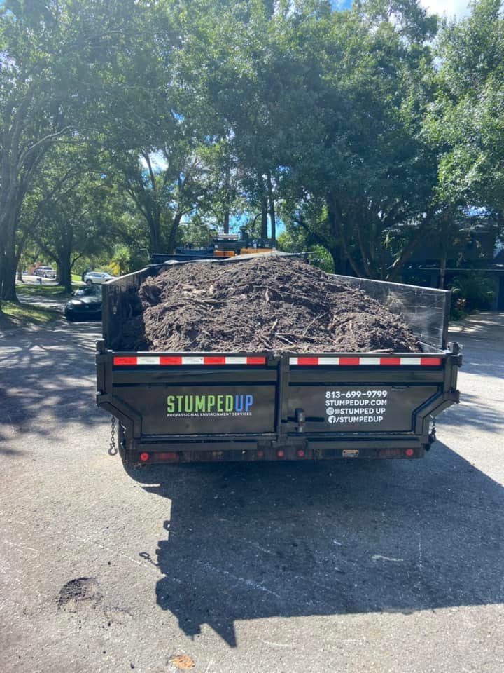 Black trailer loaded with dark mulch; STUMPED UP logo. Outdoors, sunny day.