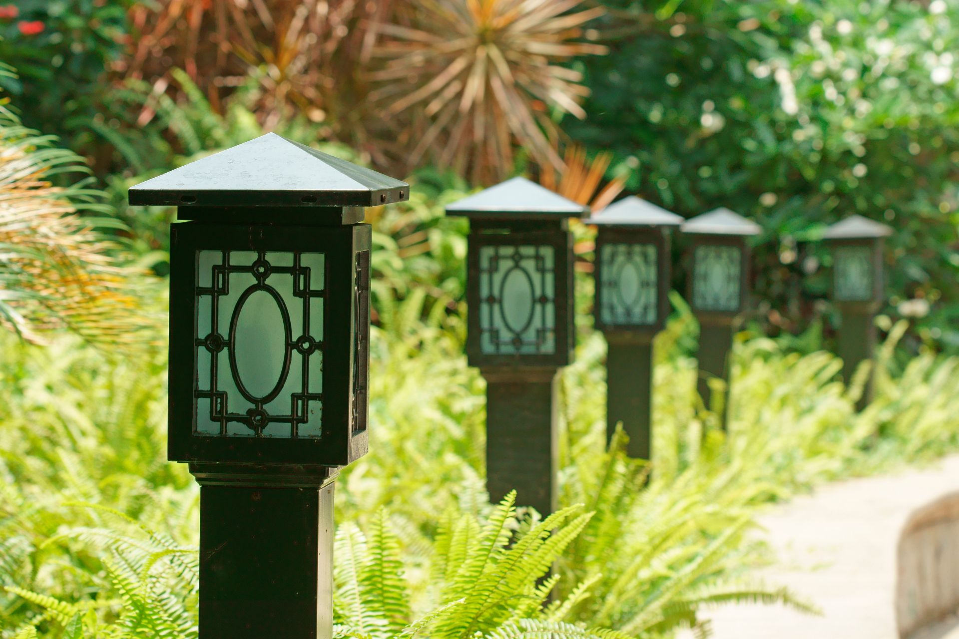 Line of black outdoor lanterns in a garden, surrounded by green foliage.