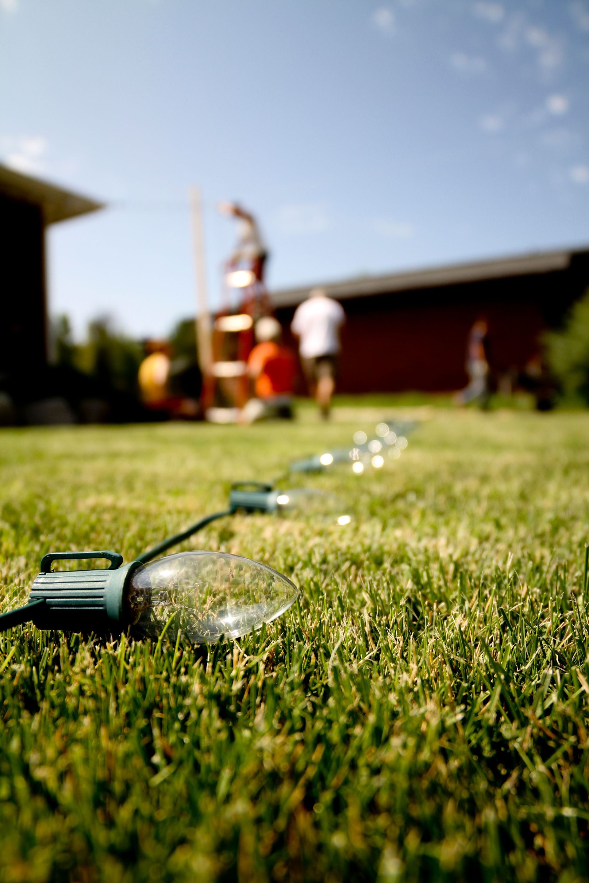 Graveyard Lawn Care Garden sprinkler watering a grassy lawn with blurred people and a house in the background