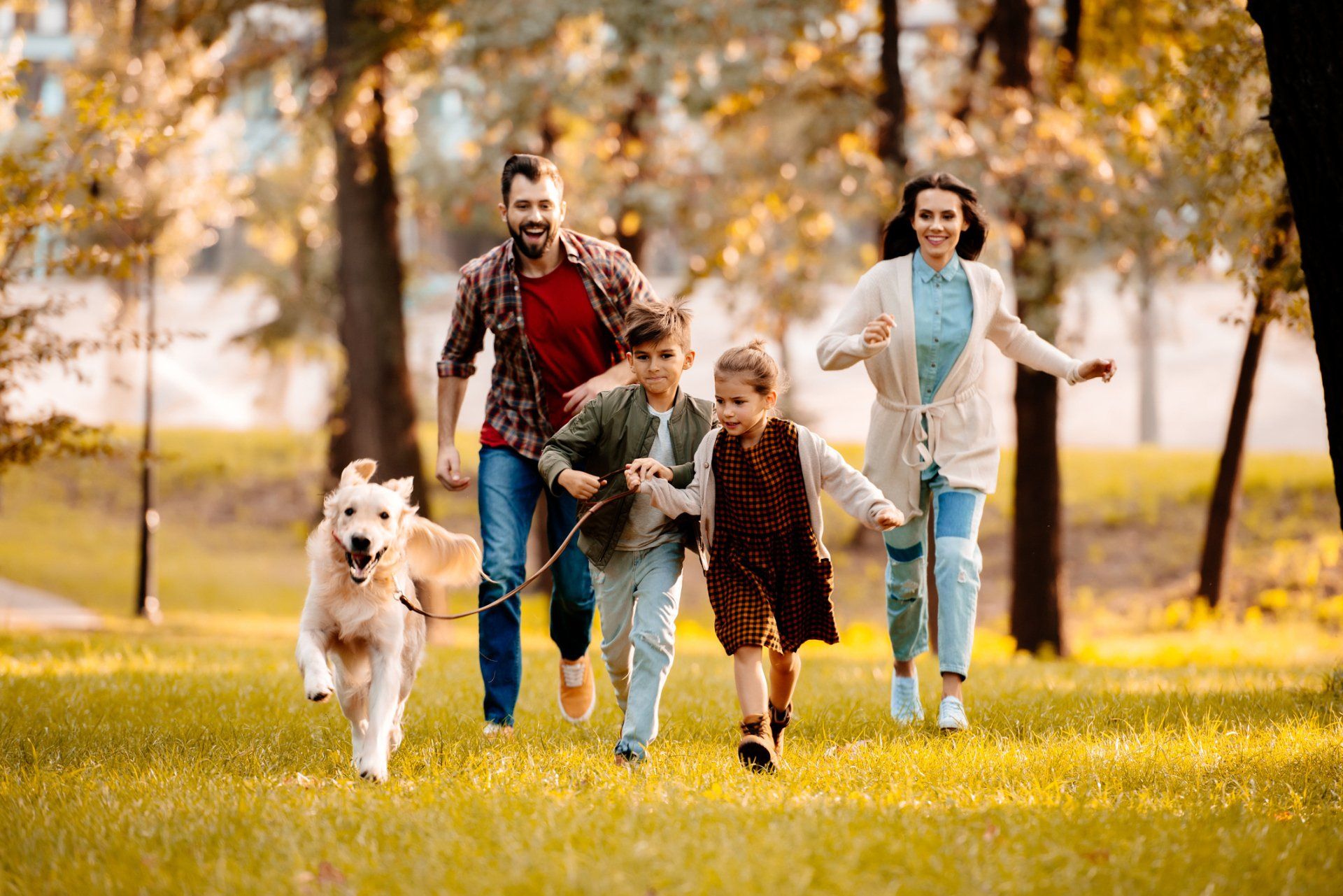 Family and dog running through a sunny autumn park