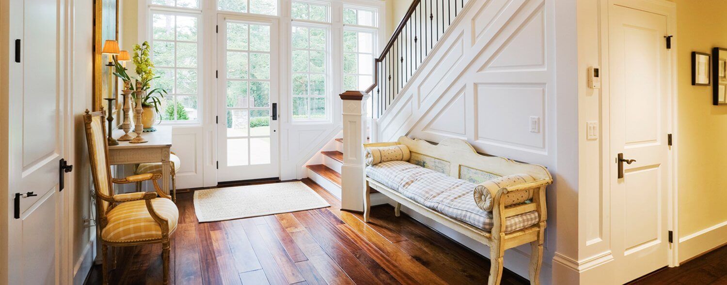 Bright entryway with white staircase, wooden floor, and bench by a window and glass doors