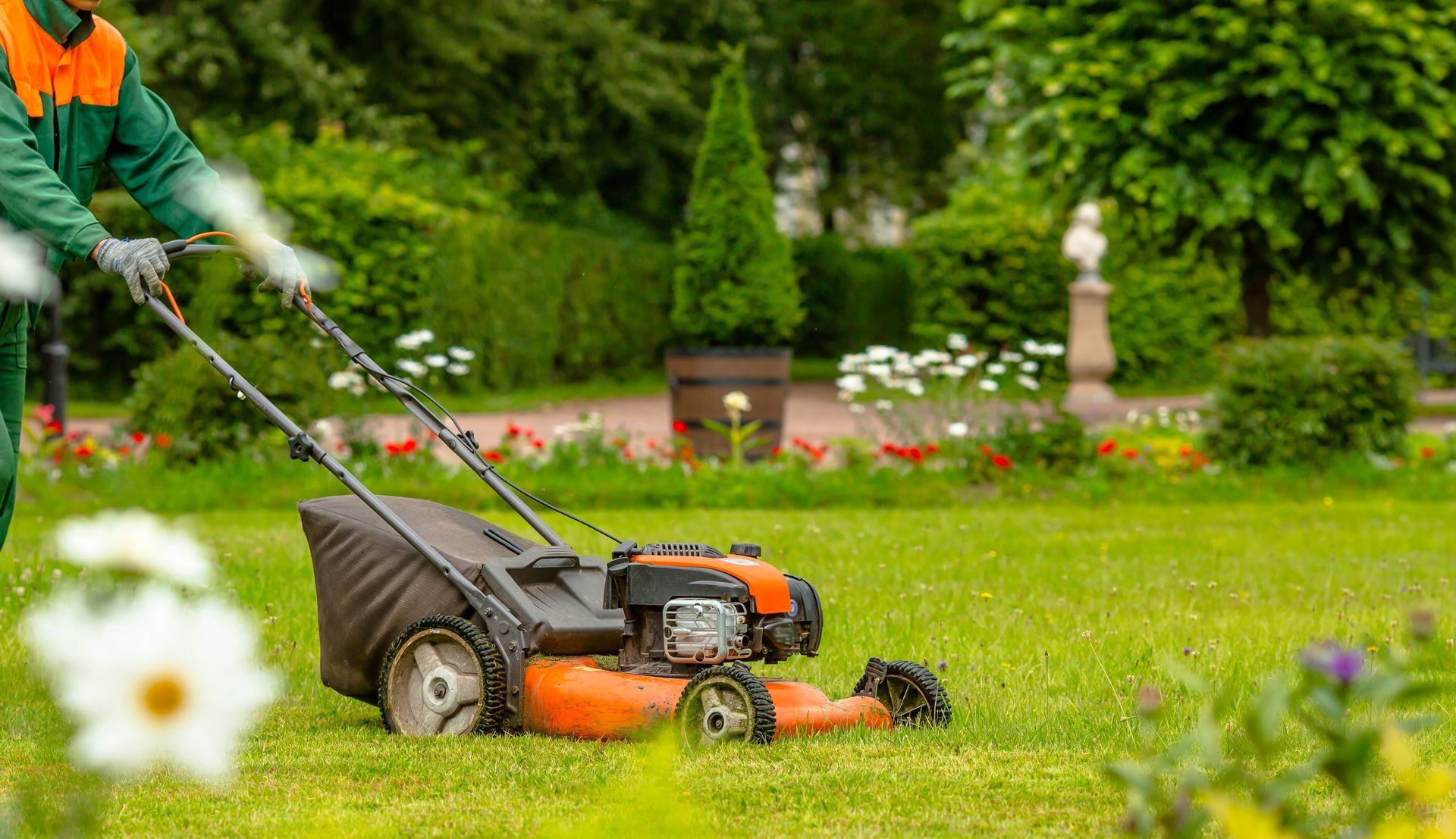 A Man is Using a Lawn Mower to Cut the Grass in a Park
