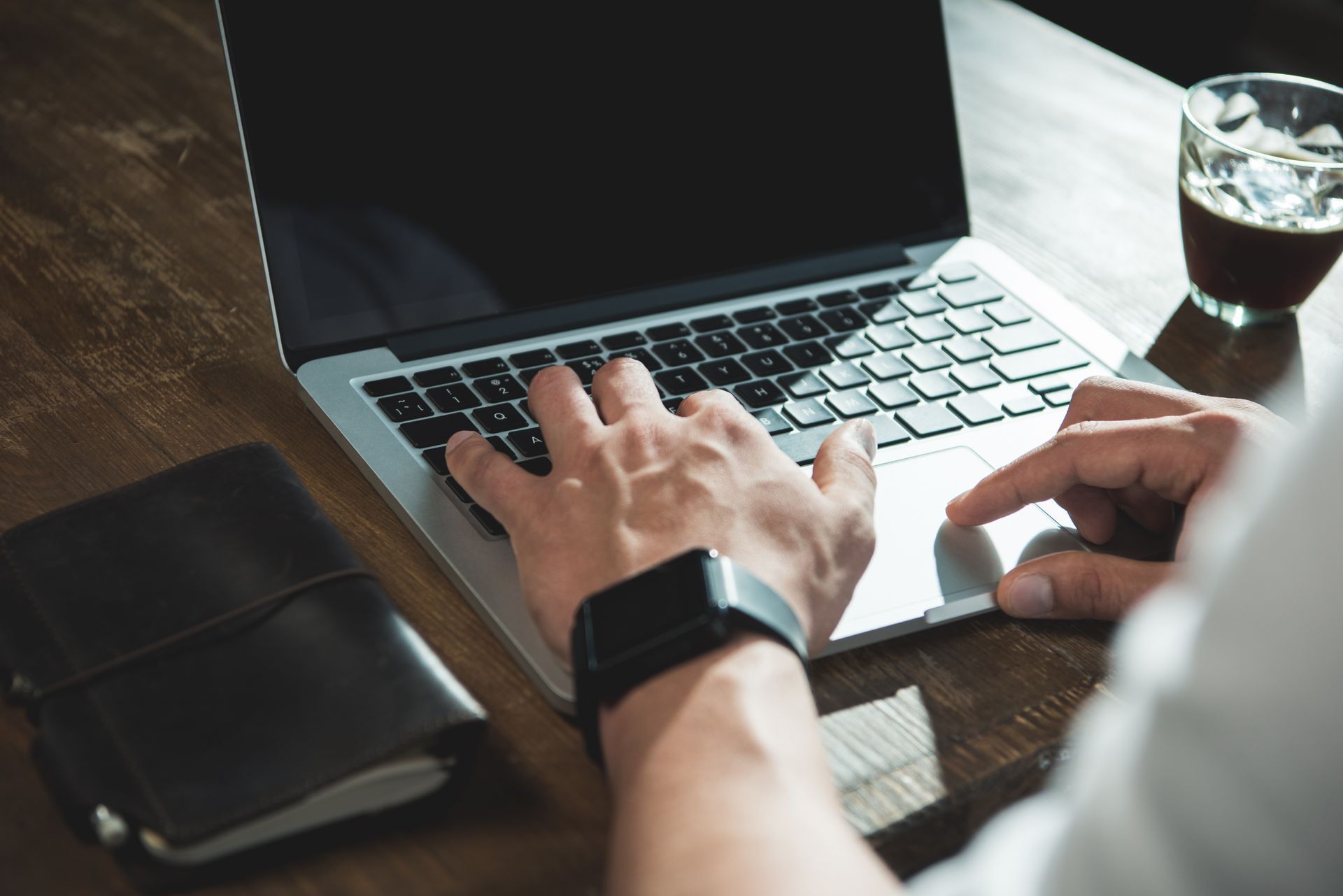 a person wearing a smart watch is typing on a laptop computer .