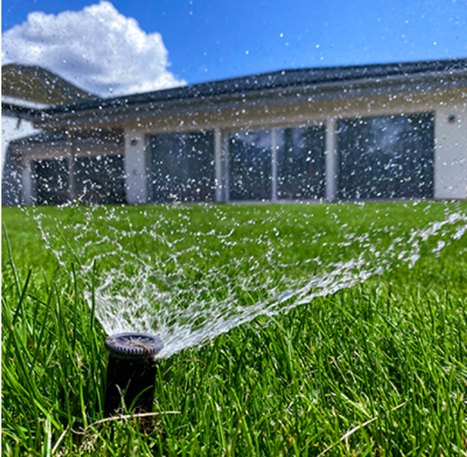 Un arroseur de pelouse pulvérisant de l'eau sur une pelouse verte luxuriante devant une maison