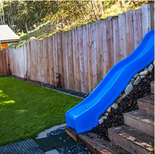 Un toboggan bleu dans une cour arrière à côté d'une clôture en bois