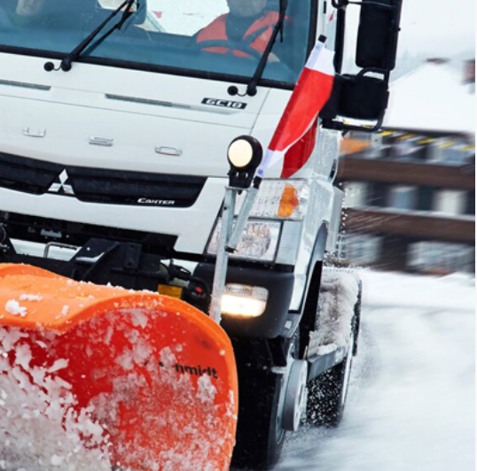 Un camion blanc avec un drapeau rouge, blanc et bleu sur le côté déneige